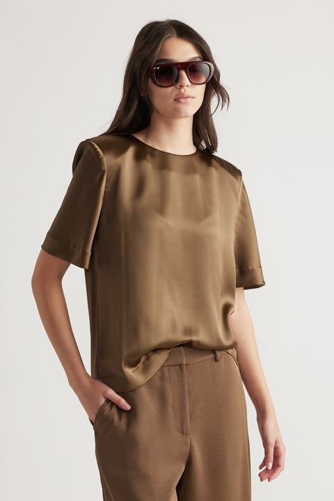 Woman wearing a bronze satin top with structured shoulders paired with matching high-waisted trousers and sunglasses