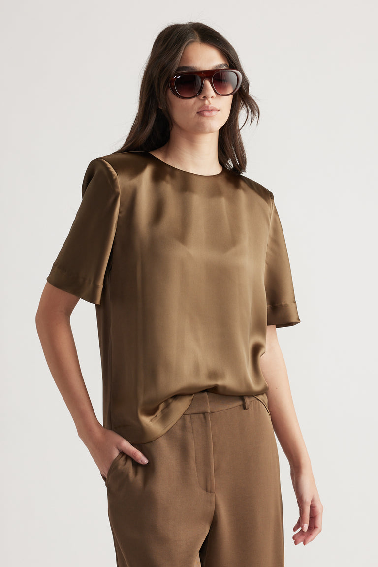Woman wearing a bronze satin top with structured shoulders paired with matching high-waisted trousers and sunglasses