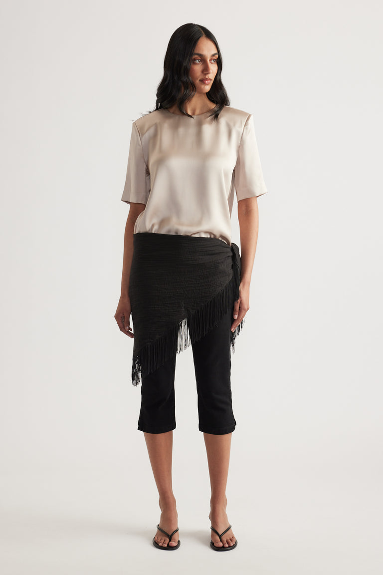 Woman wearing a satin shoulder pad top with black cropped pants and a fringed wrap skirt overlay