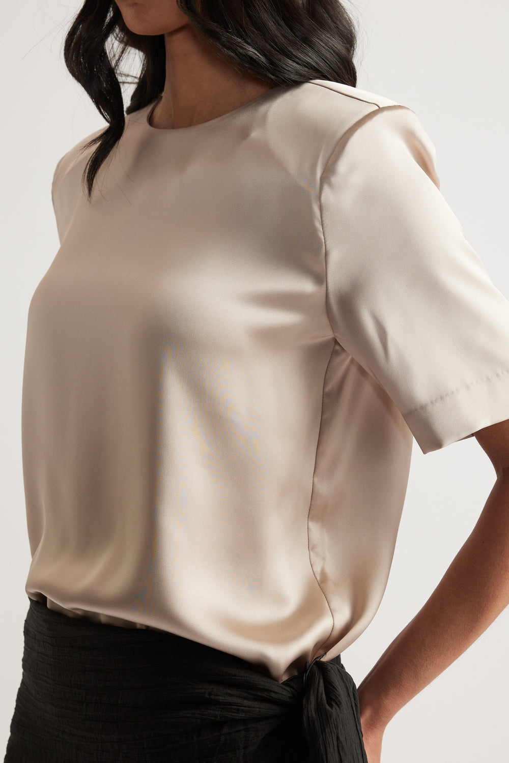 Woman wearing an ivory satin top with shoulder pads, a round neckline and short sleeves with black pants