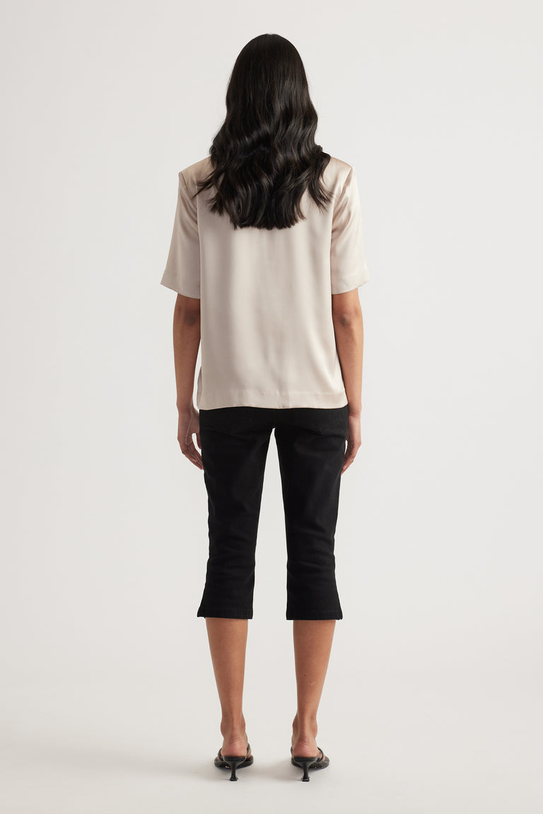 Woman viewed from behind wearing a cream satin short sleeve top with black cropped pants and heels