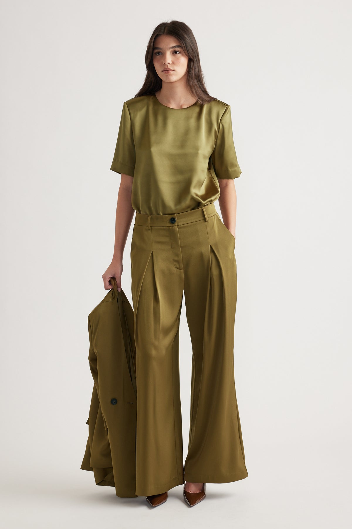 Woman wearing a chartreuse satin top with structured shoulders paired with high-waisted wide-leg trousers and pointed heels.