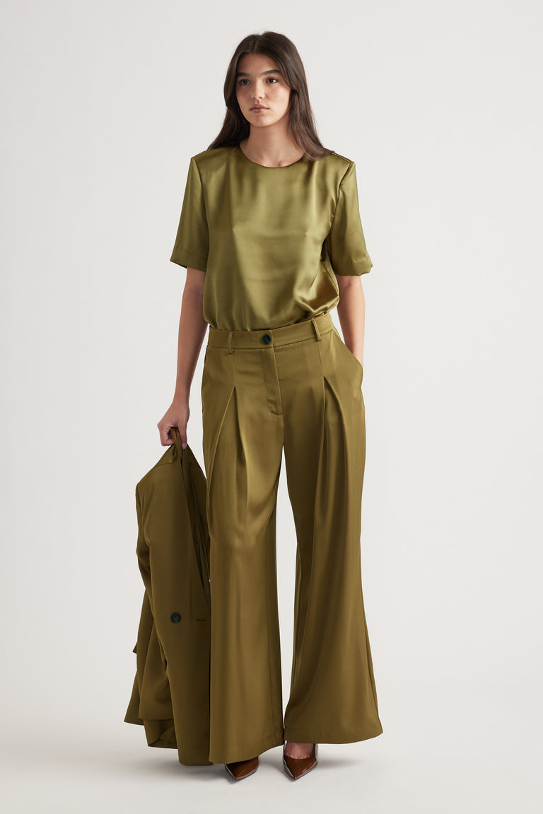 Woman wearing a chartreuse satin top with structured shoulders paired with high-waisted wide-leg trousers and pointed heels.