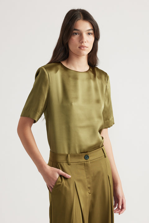 Woman wearing a satin short sleeve top with shoulder pads paired with high-waisted pleated olive trousers