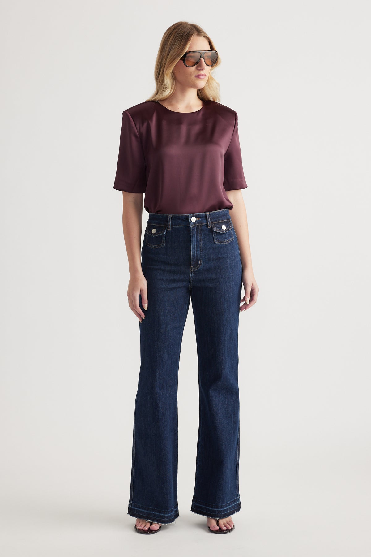 Woman wearing a burgundy satin shoulder pad top with wide leg dark denim jeans and sunglasses