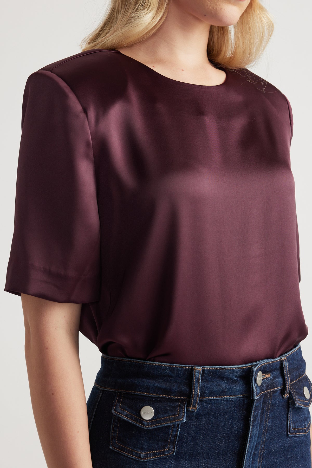 Woman wearing a burgundy satin top with shoulder pads, a round neck and short sleeves with jeans