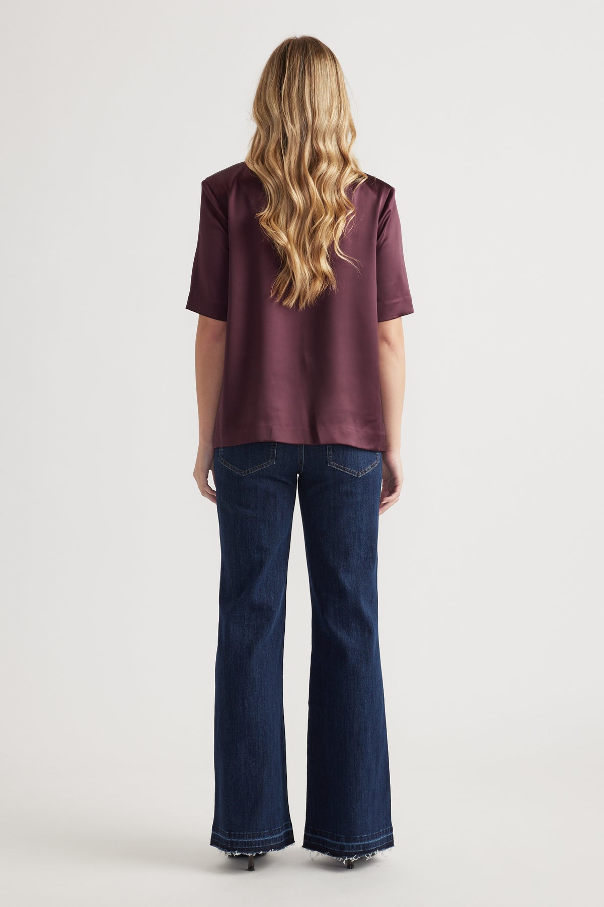 Woman wearing a burgundy satin shoulder pad top with short sleeves and wide leg jeans