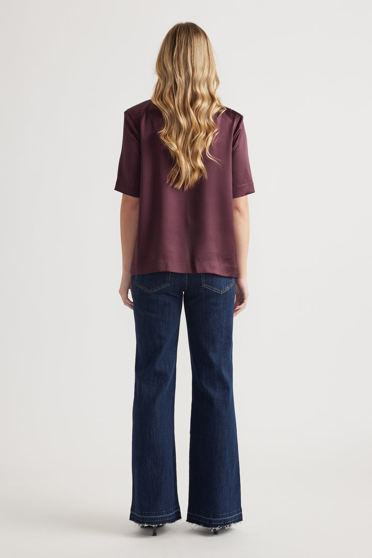Woman wearing a burgundy satin shoulder pad top with short sleeves and wide leg jeans
