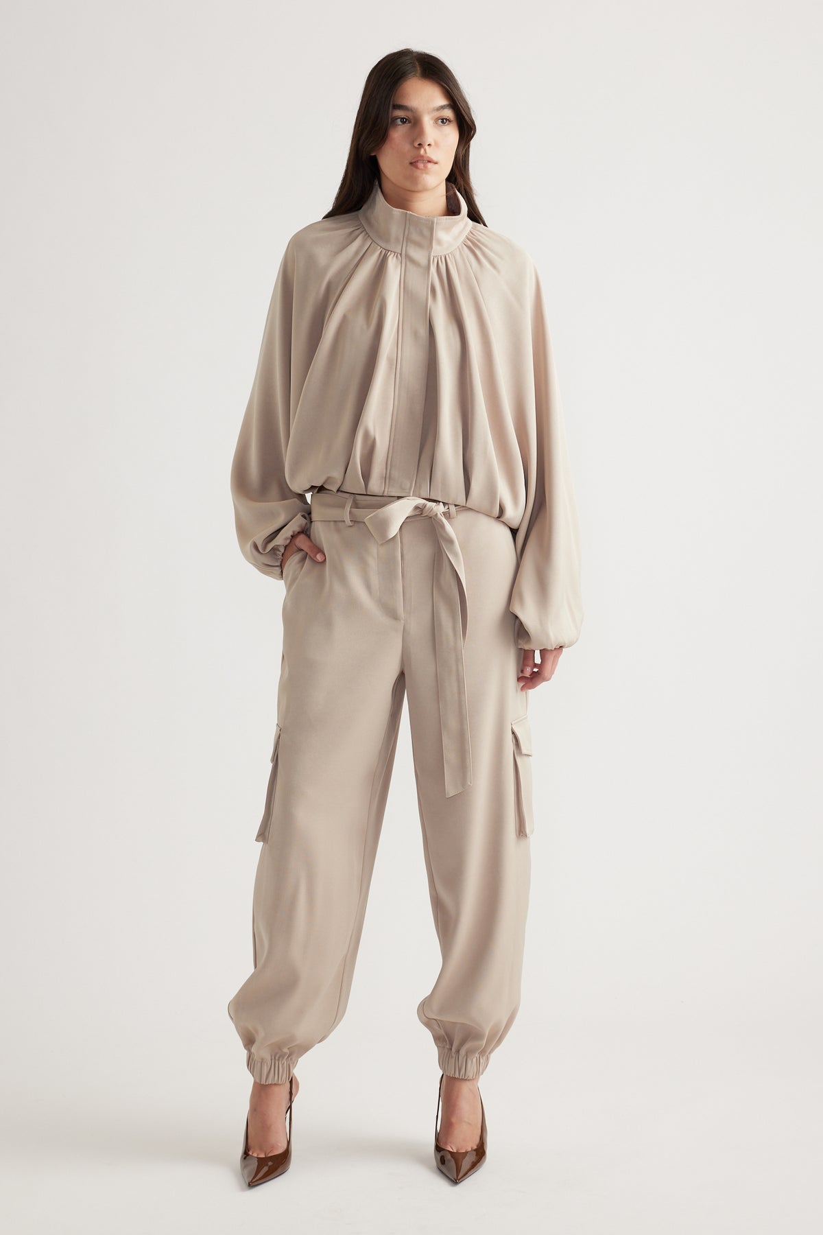 Woman wearing relaxed beige satin cargo pants with tie waist and elastic cuffs, styled with a matching loose blouse and heels