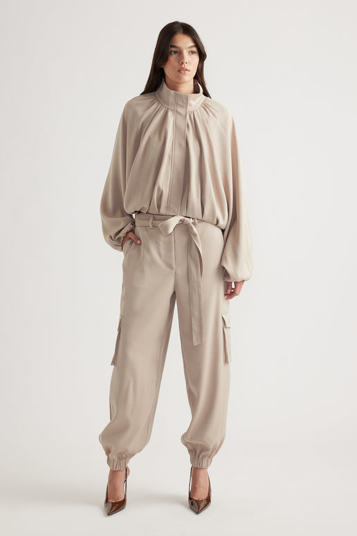Woman wearing relaxed beige satin cargo pants with tie waist and elastic cuffs, styled with a matching loose blouse and heels