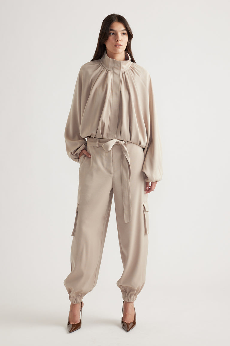 Woman wearing relaxed beige satin cargo pants with tie waist and elastic cuffs, styled with a matching loose blouse and heels