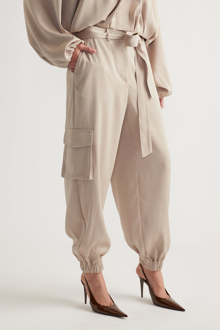 Close-up of woman wearing light beige satin cargo pants with gathered cuffs and side pockets styled with brown pointed heels