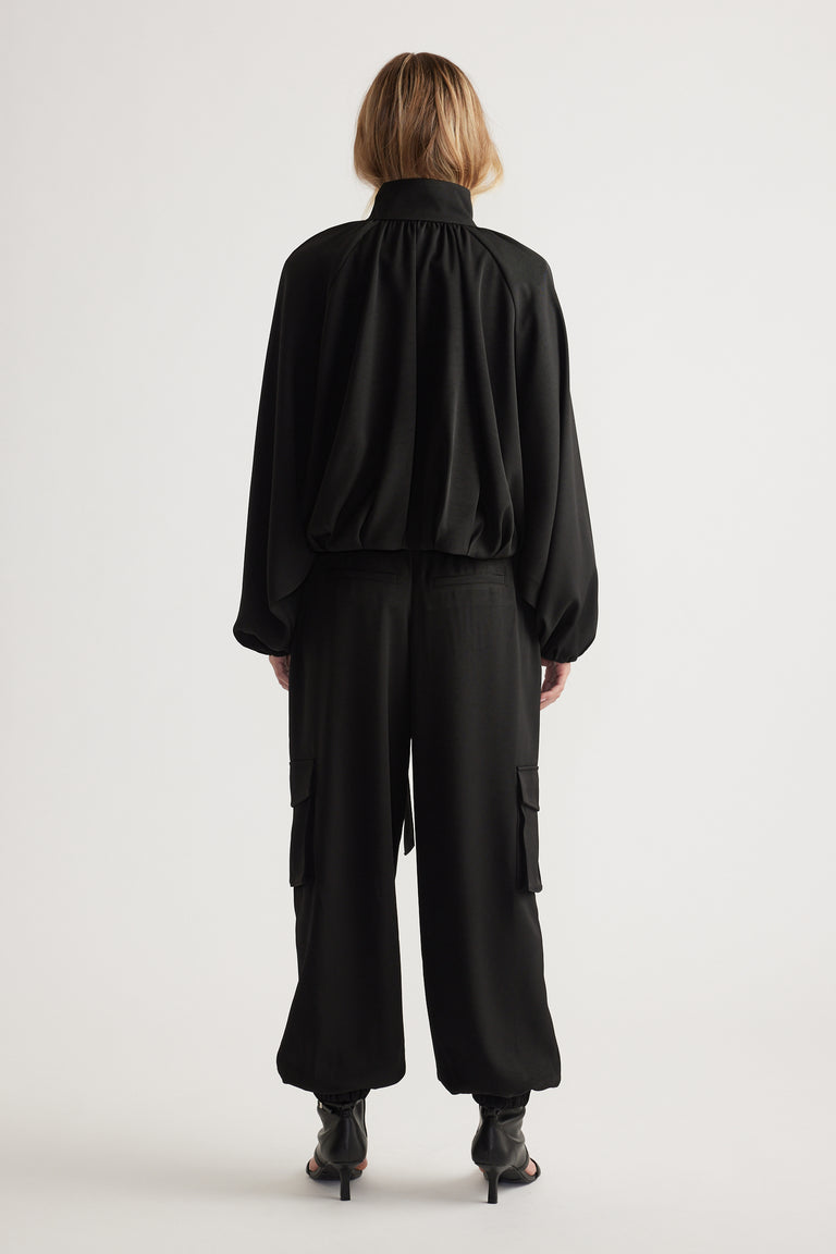 Back view of a woman wearing loose black satin cargo pants paired with a billowy long-sleeve top and open-toe heels