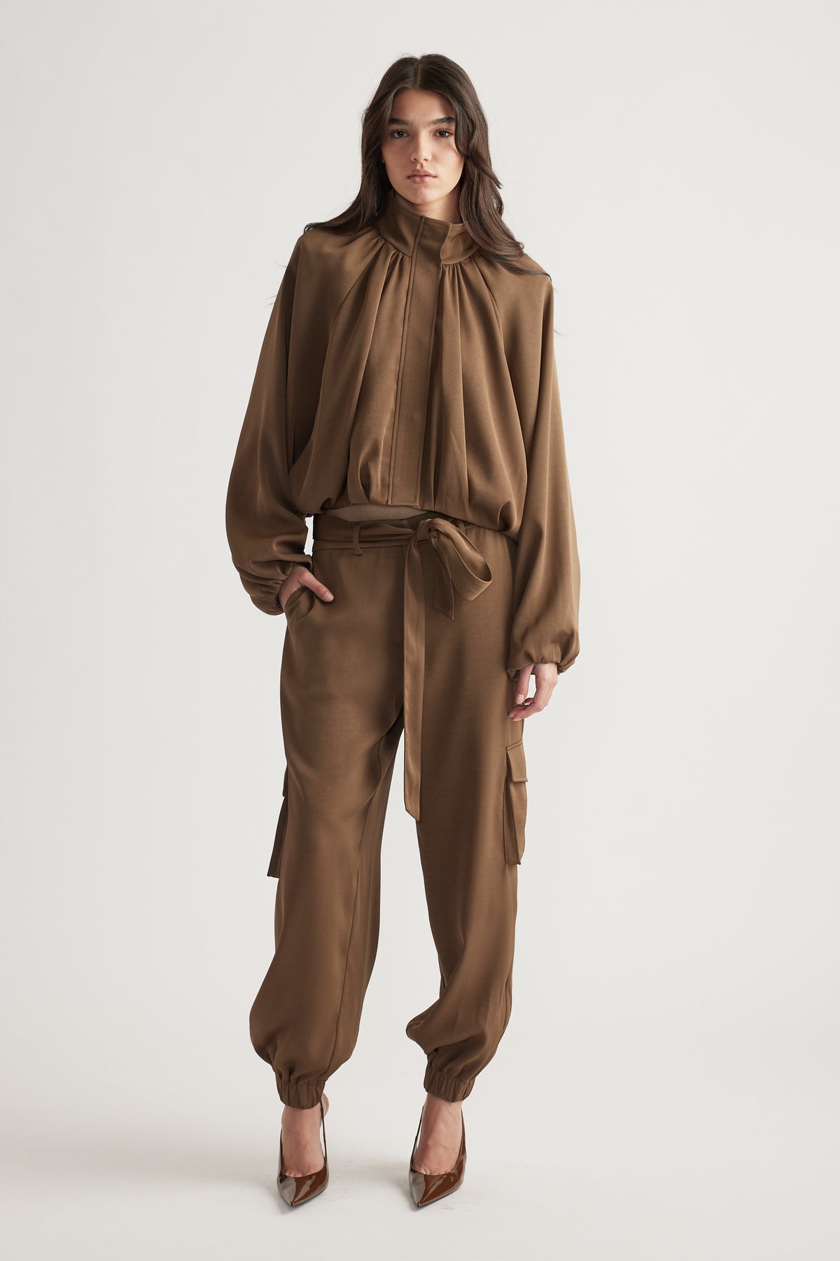 Woman wearing relaxed-fit bronze satin cargo pants with a tied waist belt and cuffed ankles styled with a matching blouse