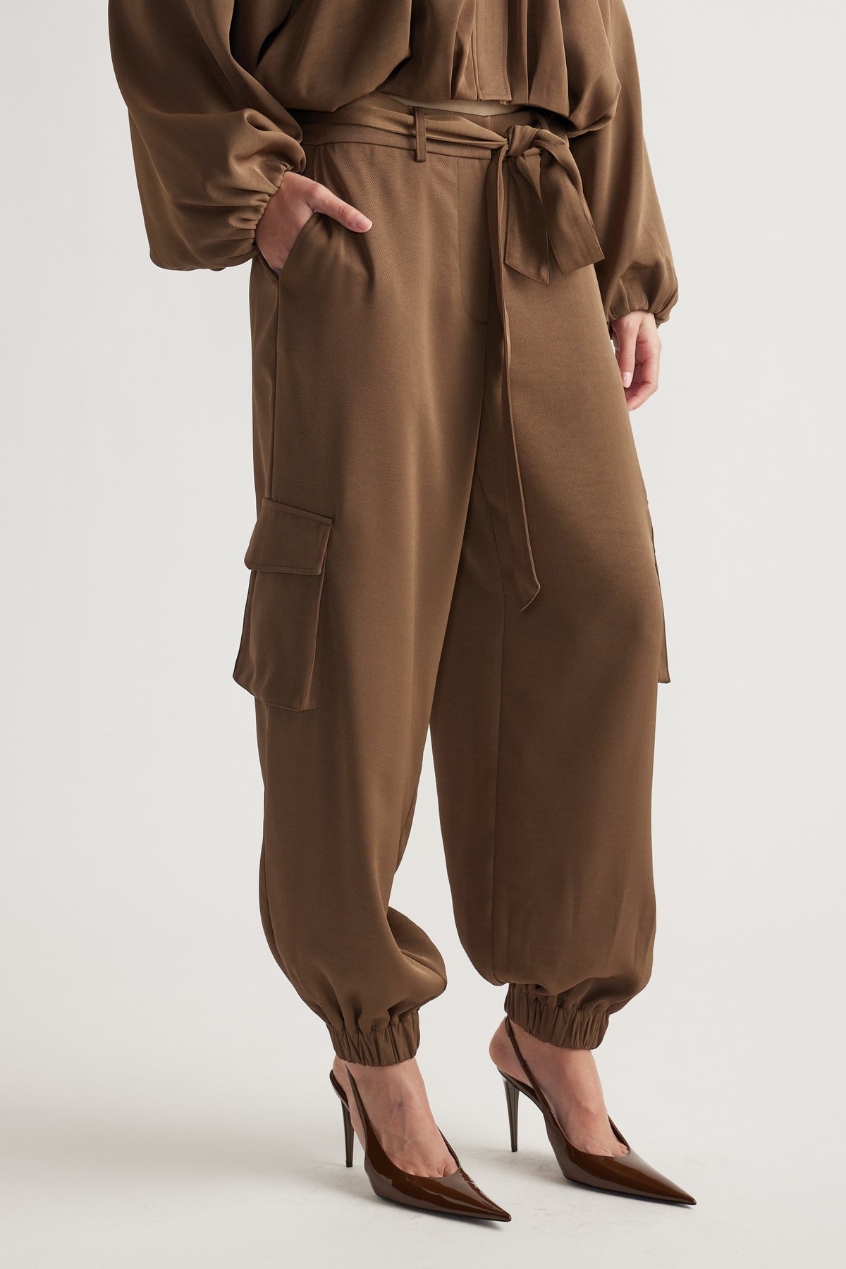 Brown satin cargo pants with elastic cuffs and side pockets, styled with pointed high-heeled shoes for a polished look.