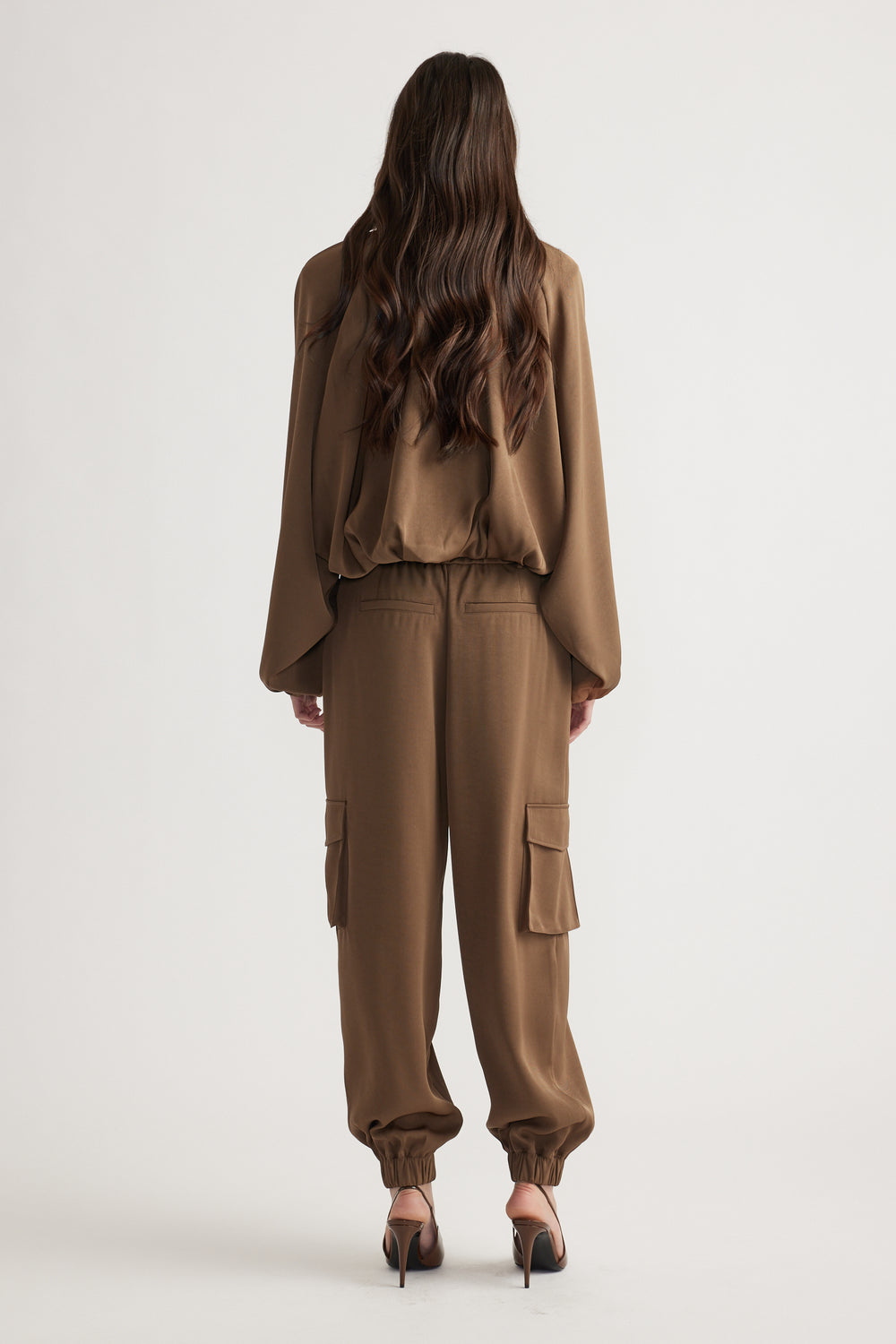 Back view of relaxed fit satin cargo pants in warm bronze with cuffed ankles and flap pockets, styled with matching top