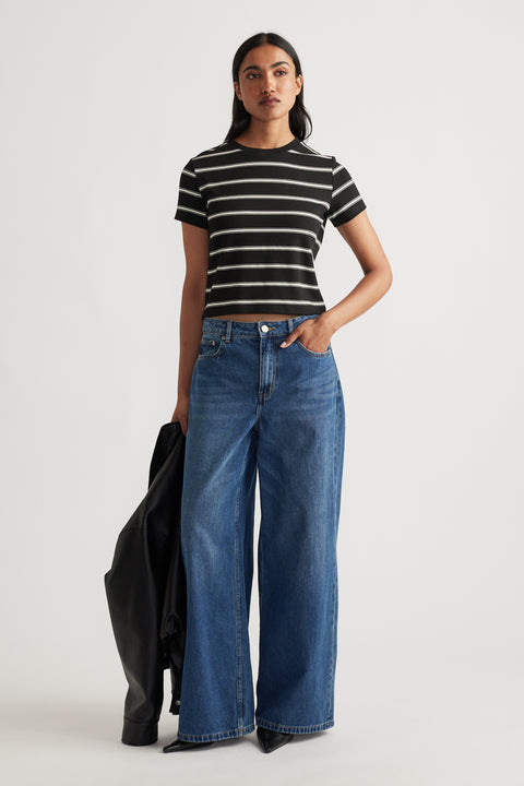 Woman wearing a cropped black and white striped tee paired with high-waisted wide-leg blue denim jeans holding a black jacket