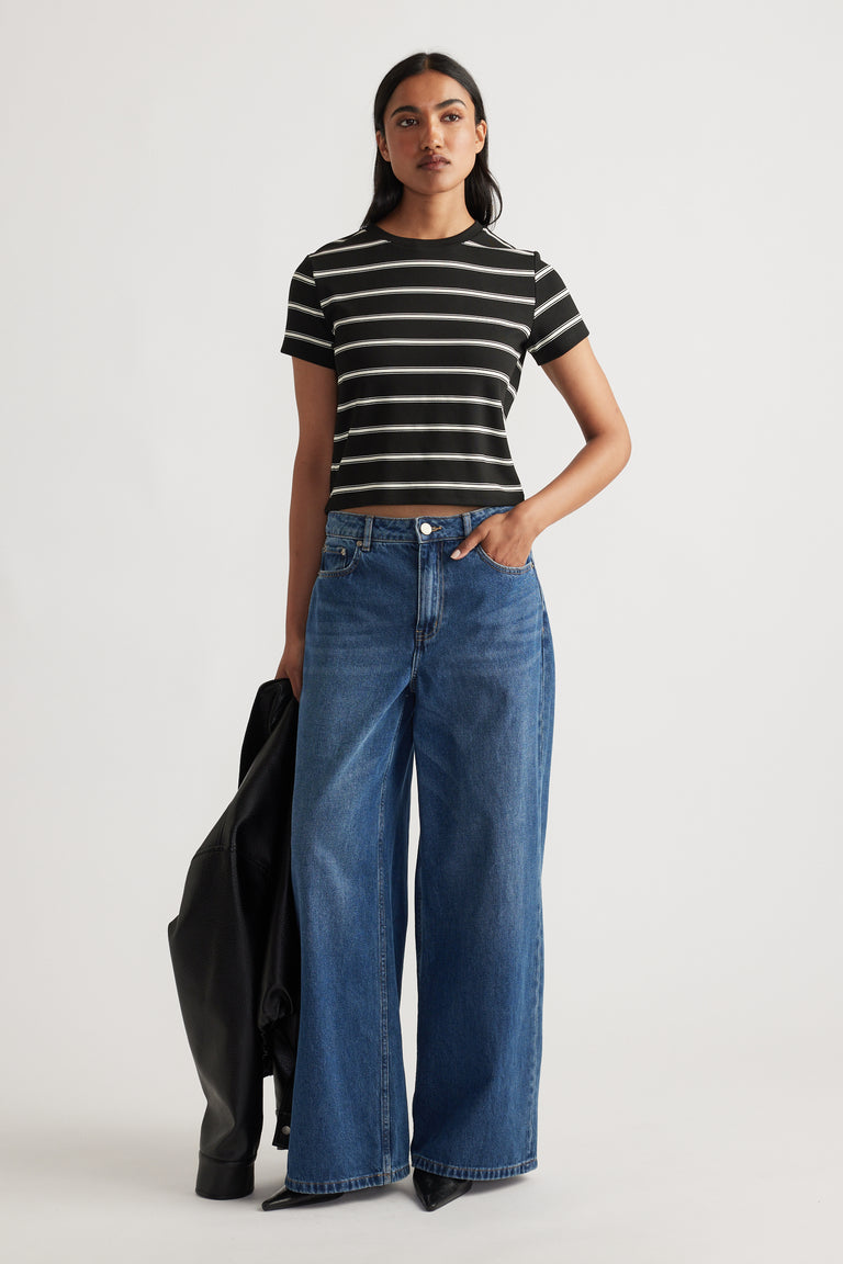 Woman wearing a cropped black and white striped tee paired with high-waisted wide-leg blue denim jeans holding a black jacket