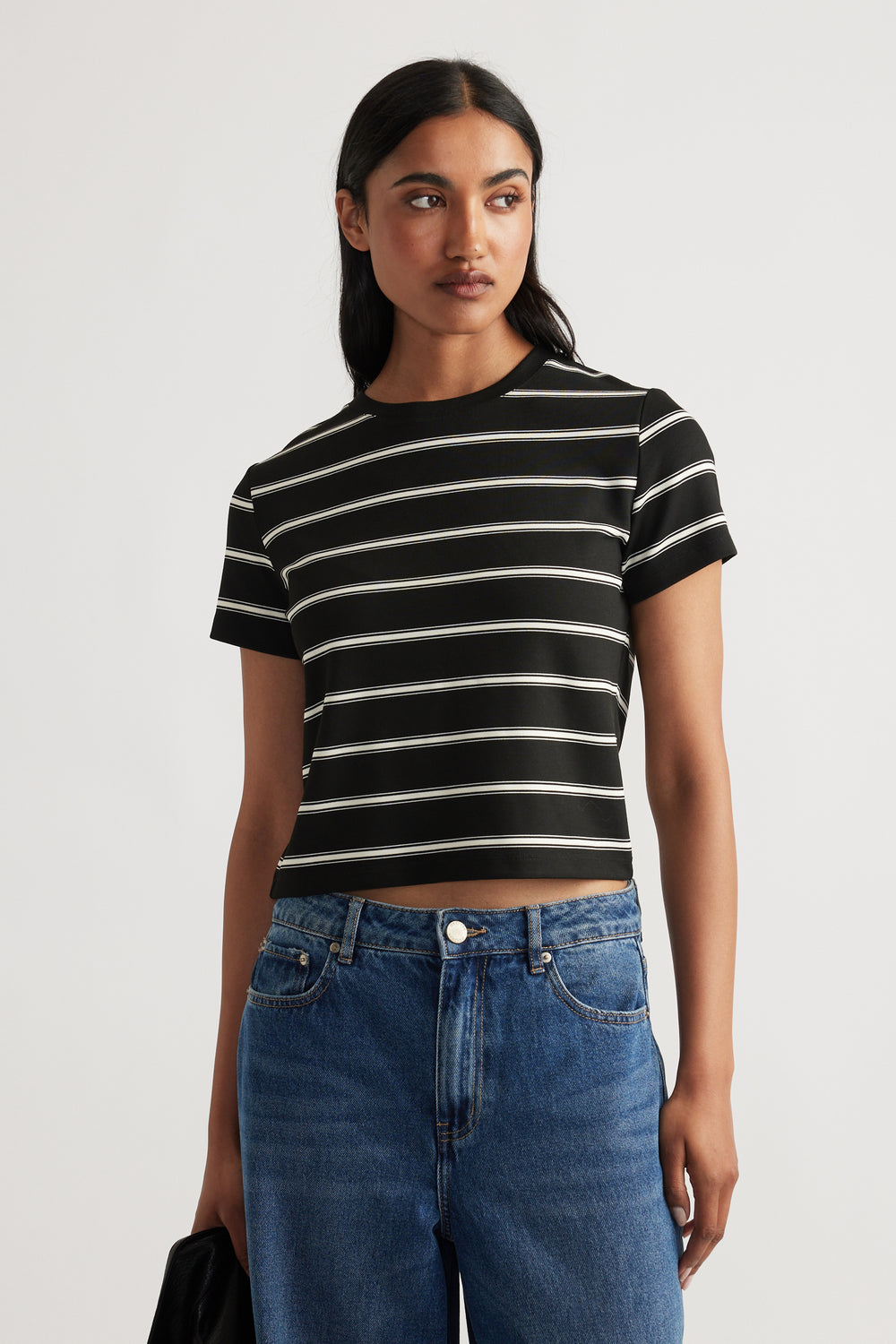 Front view of a black mini tee with white stripes, paired with high-waisted blue denim jeans for a casual look