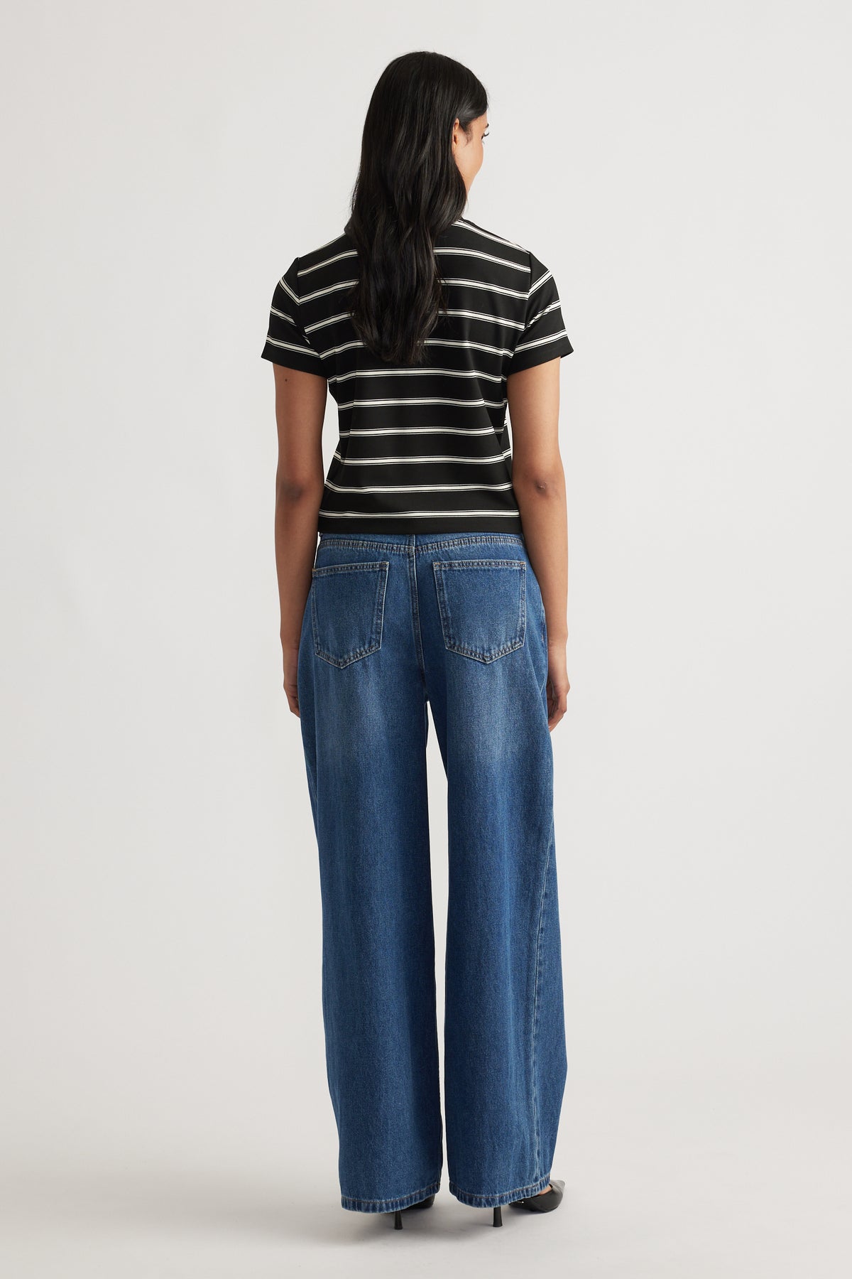 Woman wearing a black and white striped mini tee paired with relaxed wide-leg blue denim jeans and black heels