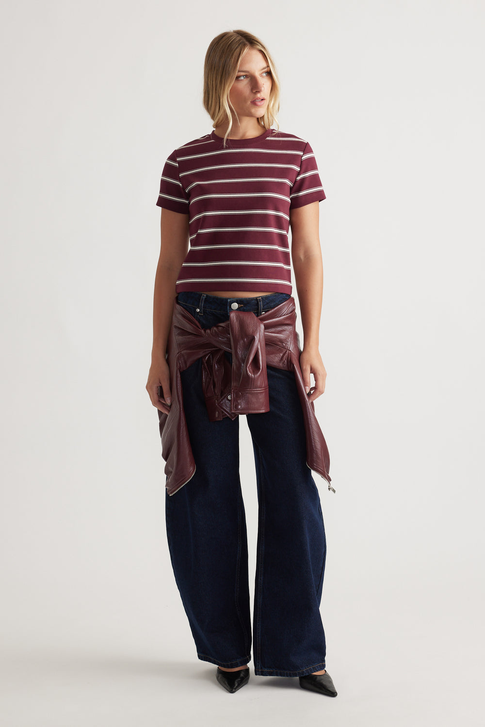 Woman wearing a plum striped cropped tee paired with wide-leg dark denim jeans and a tied maroon leather jacket