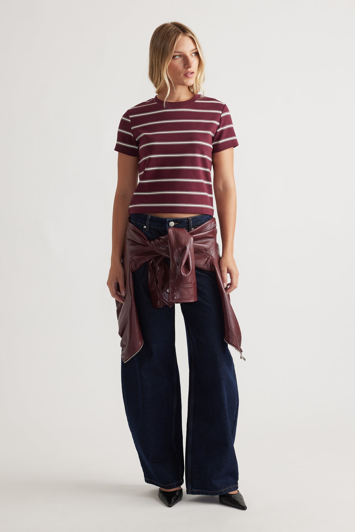 Woman wearing a plum striped cropped tee paired with wide-leg dark denim jeans and a tied maroon leather jacket