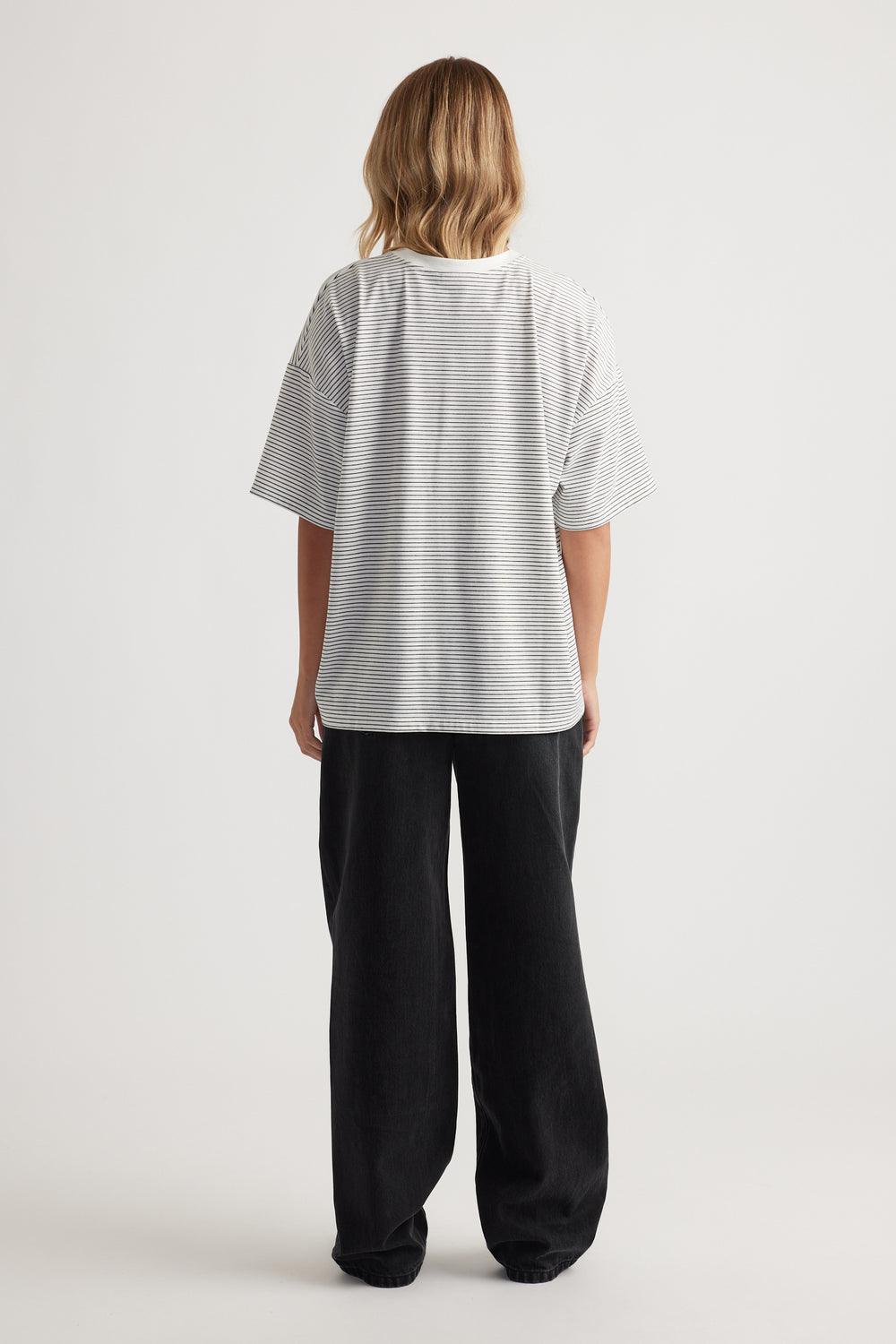 Woman standing facing away wearing a loose white striped short-sleeve top and wide-leg black pants