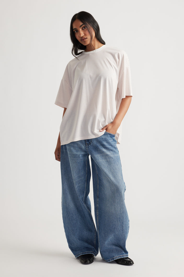 Woman wearing a loose pale pink short-sleeve top paired with wide-leg blue denim jeans and black shoes