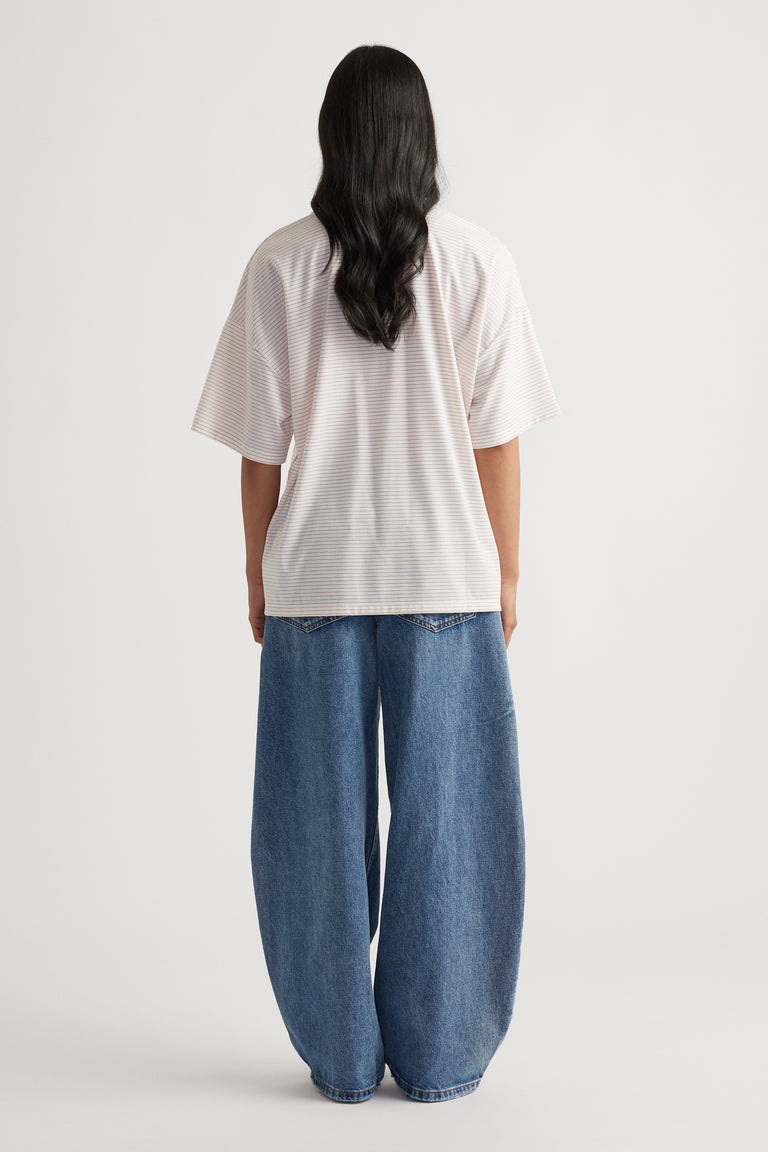 Woman seen from behind wearing a loose white short-sleeve top paired with wide-leg blue denim jeans standing on a neutral background