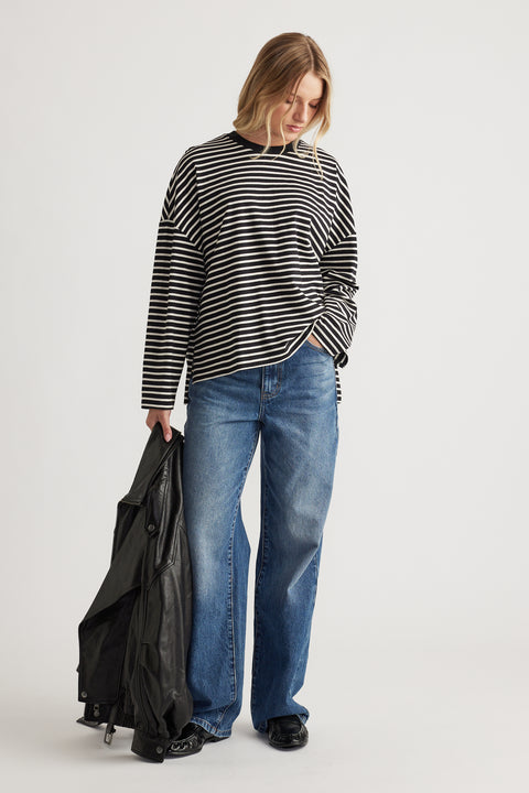 Woman wearing a relaxed black and ivory striped long sleeve top paired with classic blue wide-leg jeans and holding a leather jacket