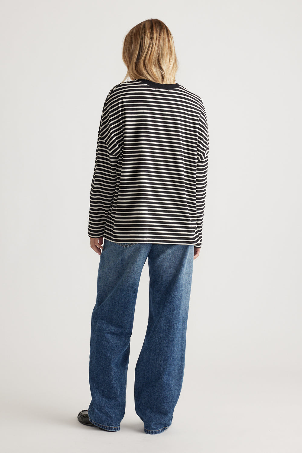 Woman wearing a relaxed black and cream striped long sleeve top with wide-leg blue jeans for a casual look