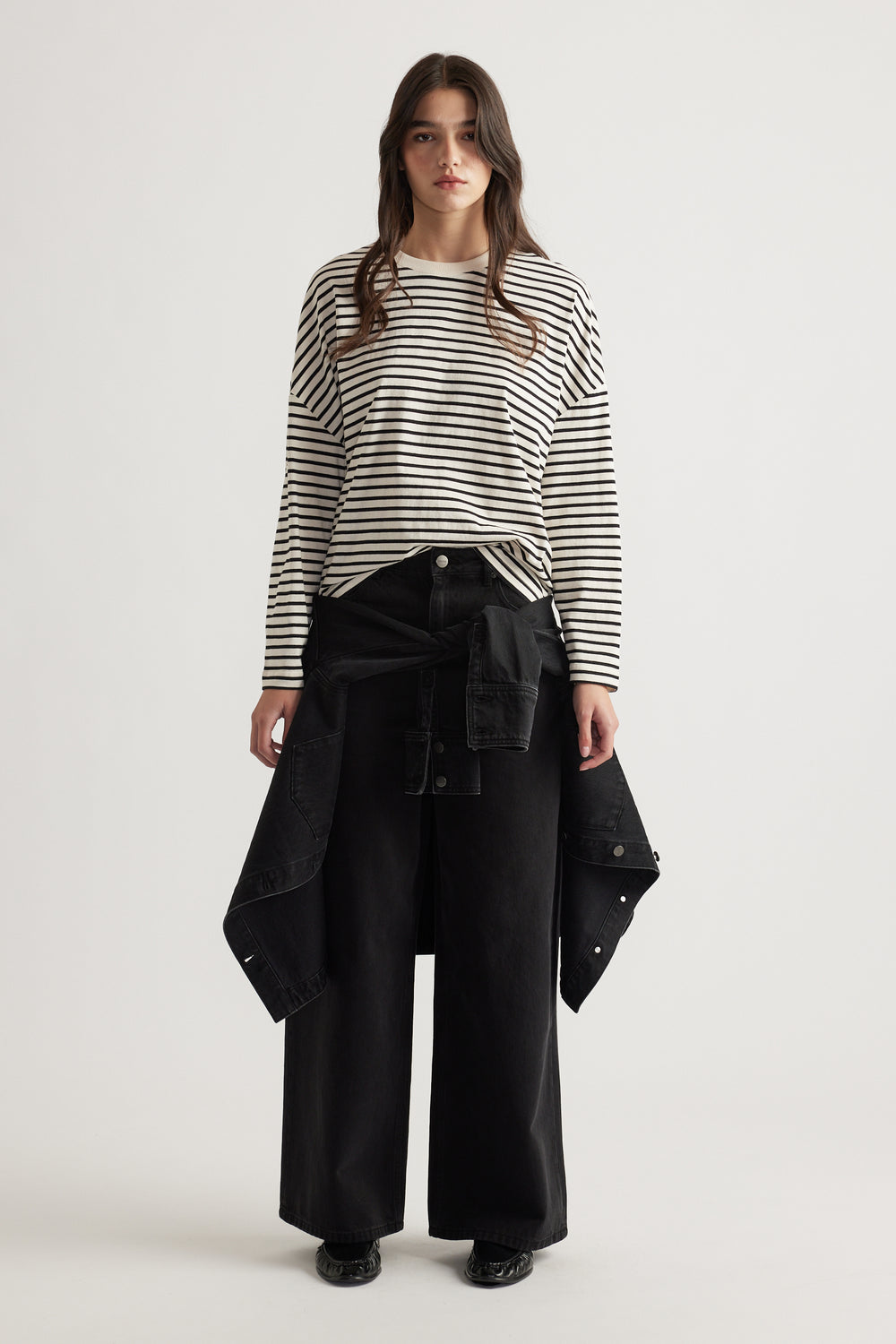 Woman wearing a relaxed striped long sleeve top paired with wide-leg black pants and a black jacket tied at the waist