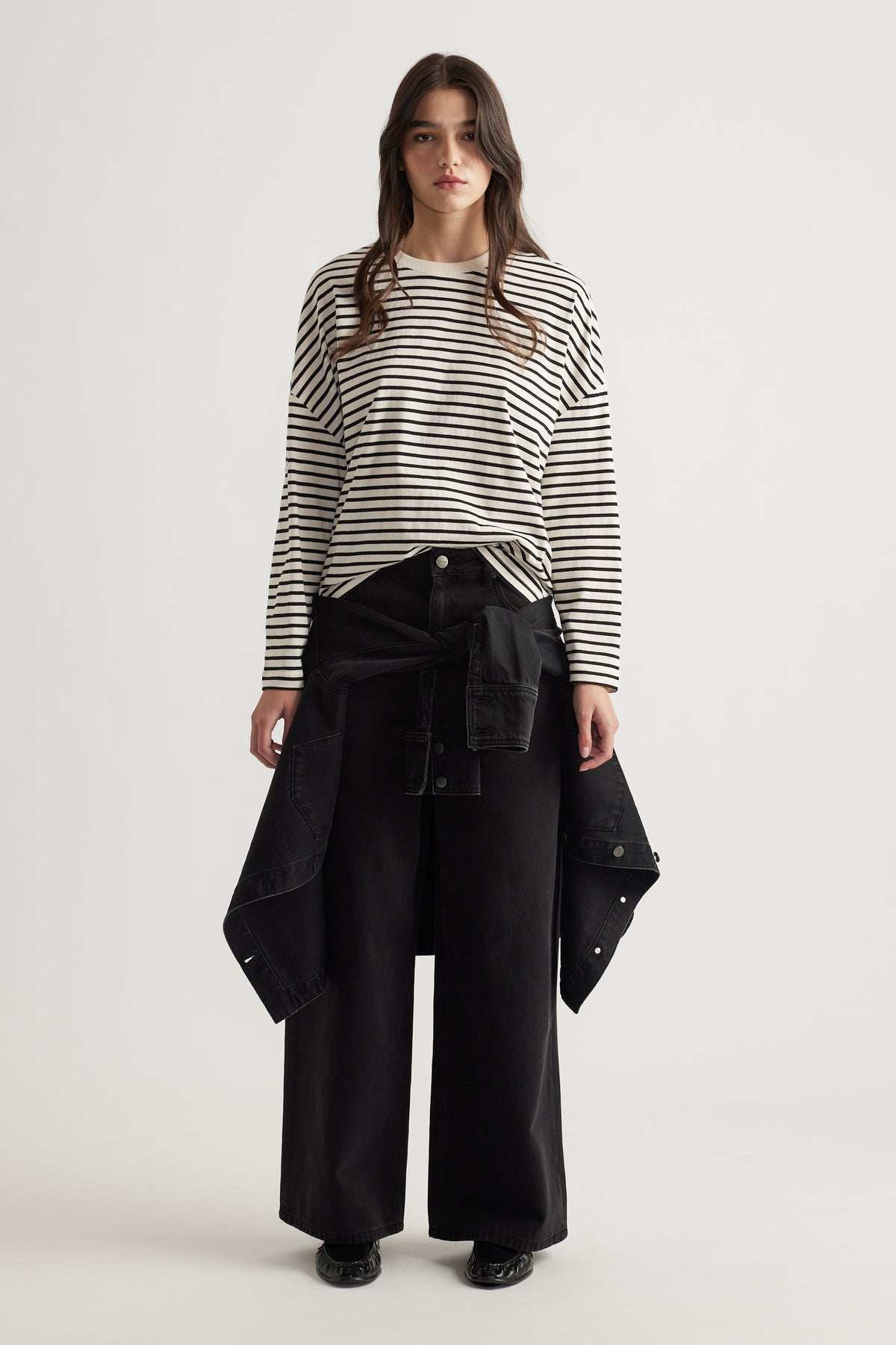 Woman wearing a relaxed striped long sleeve top paired with wide-leg black pants and a black jacket tied at the waist