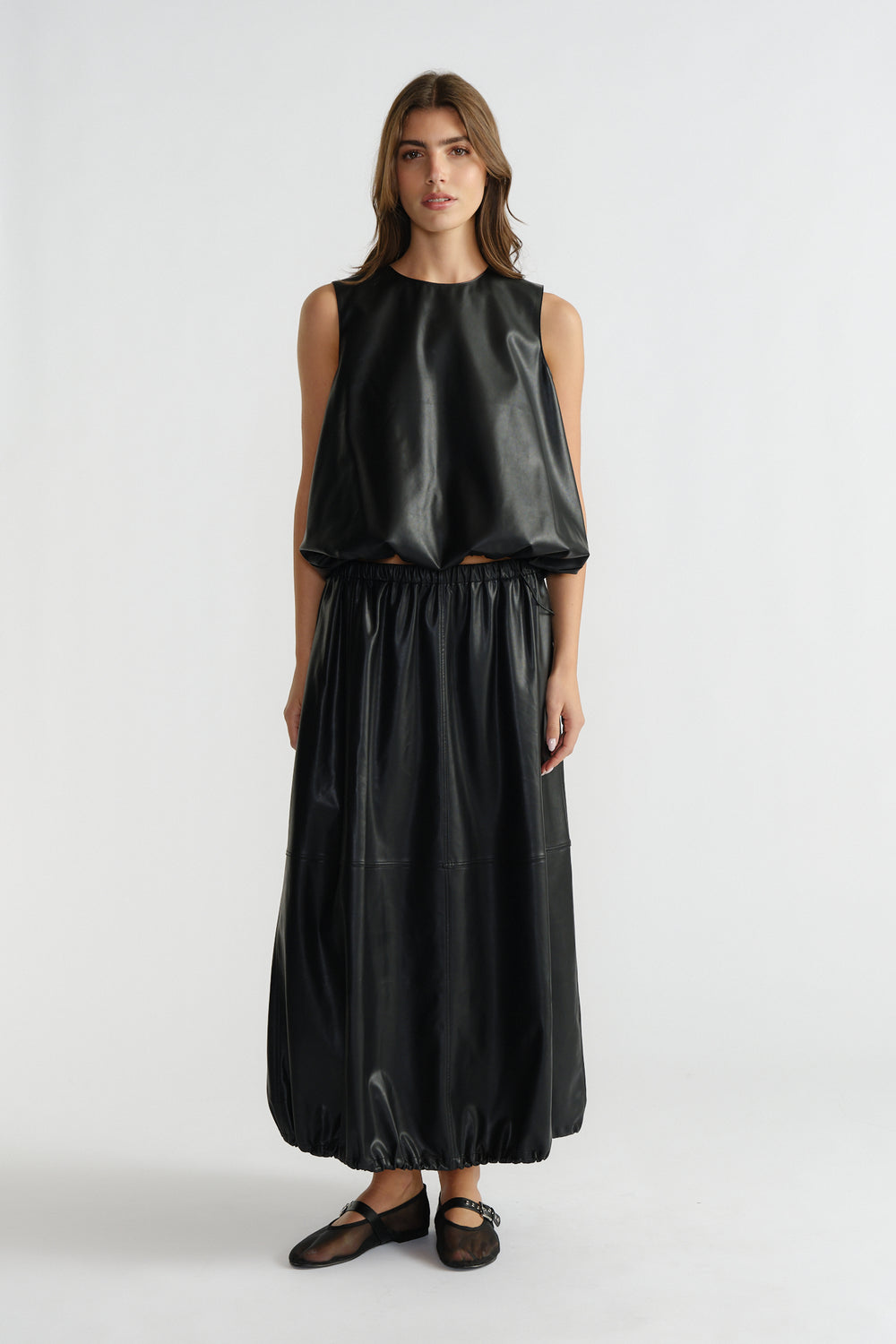 Woman wearing a sleeveless black faux leather top with a gathered hem paired with a matching long skirt