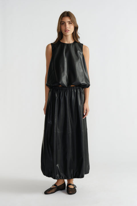 Woman wearing a sleeveless black faux leather top with a gathered hem paired with a matching long skirt