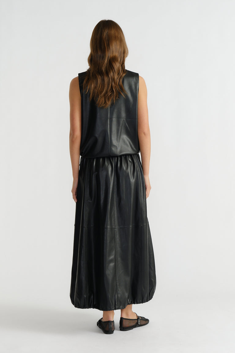 Back view of woman wearing a sleeveless black faux leather top paired with a matching gathered midi skirt and flats