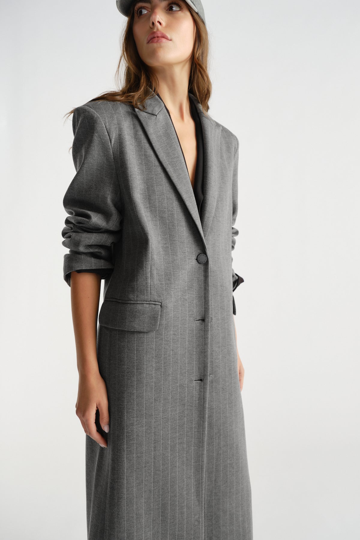 Woman wearing a tailored charcoal grey pinstripe blazer coat with ruched sleeves and a single-button closure