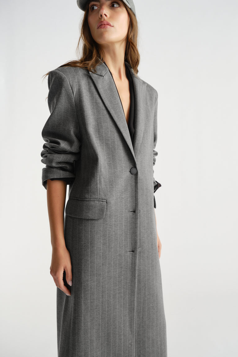 Woman wearing a tailored charcoal grey pinstripe blazer coat with ruched sleeves and a single-button closure