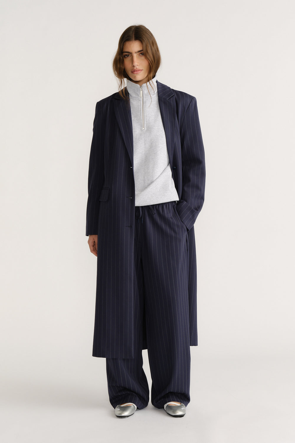 Woman wearing a navy pinstripe long blazer coat with matching wide-leg pants and a light zip-up top for a polished look