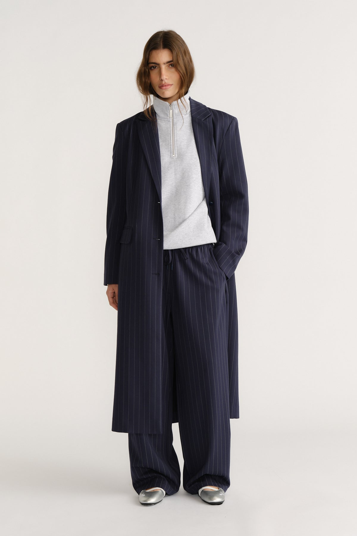 Woman wearing a navy pinstripe long blazer coat with matching wide-leg pants and a light zip-up top for a polished look