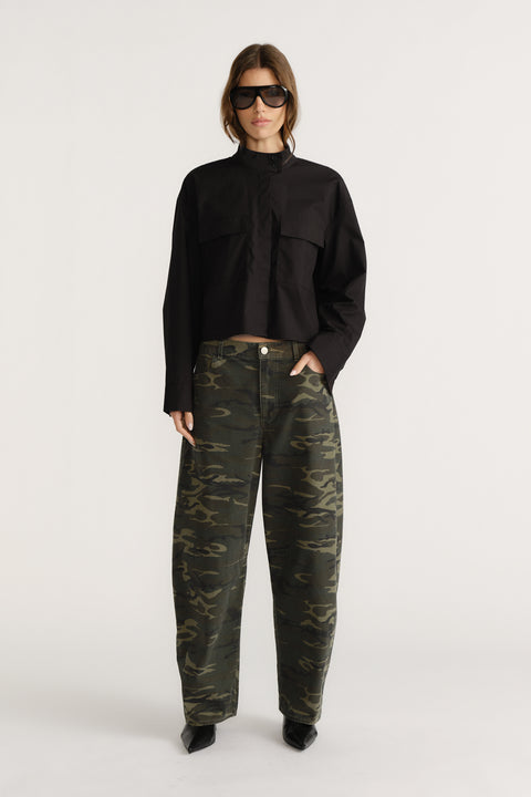 Woman wearing a cropped black utility shirt styled with loose-fitting camo pants and black pointed boots, accessorized with sunglasses.
