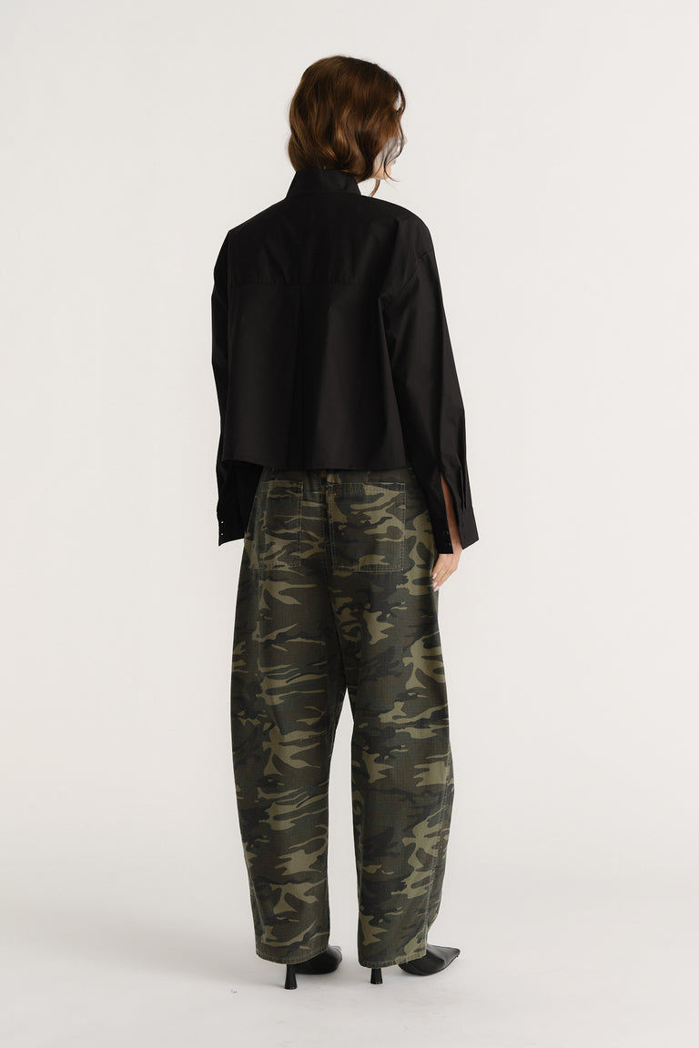 Woman seen from behind wearing a black oversized shirt and loose camouflage pants with black heeled boots.