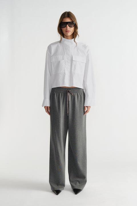 Woman wearing a white cropped utility shirt with chest pockets, paired with loose grey drawstring pants and black sunglasses.