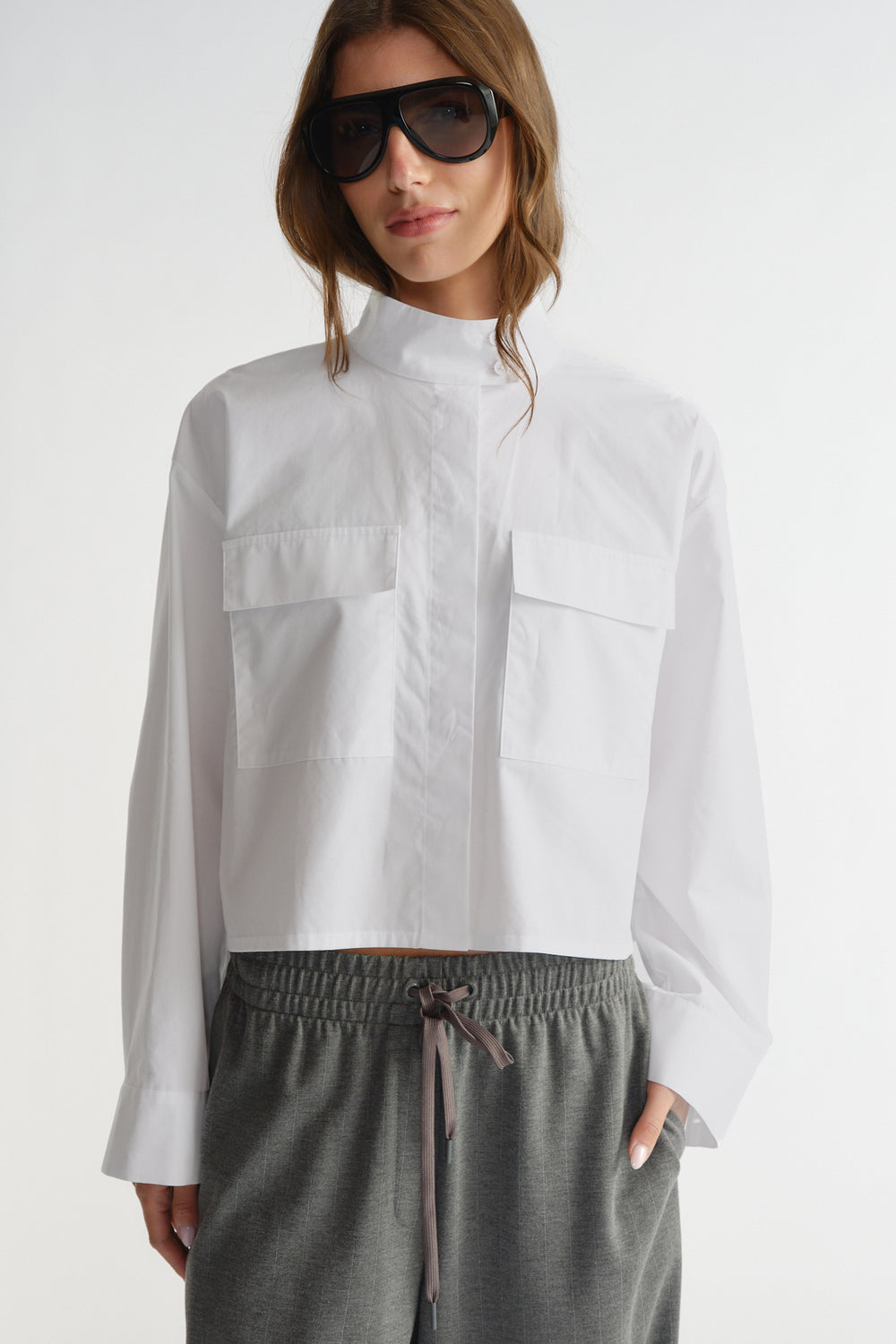 Woman wearing a crisp white cropped utility shirt with flap pockets paired with comfortable grey drawstring pants.