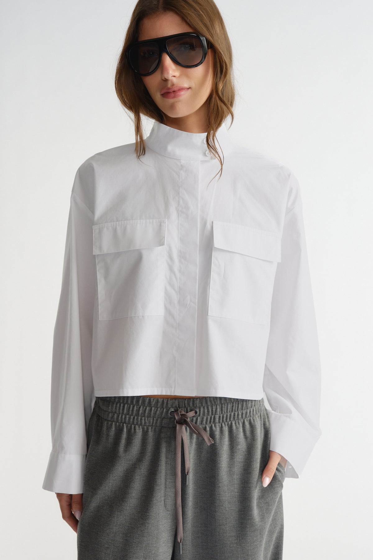 Woman wearing a crisp white cropped utility shirt with flap pockets paired with comfortable grey drawstring pants.