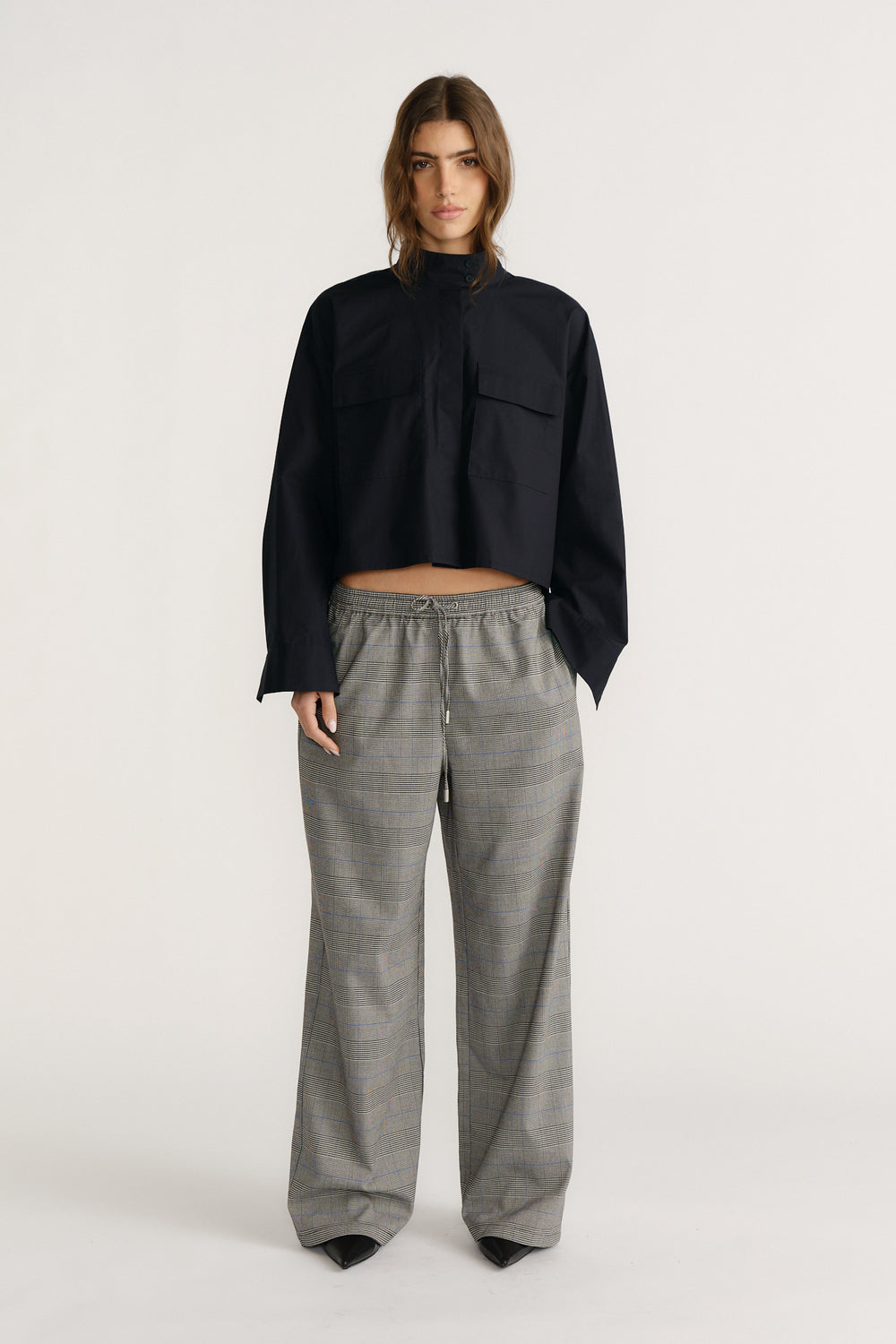 Woman wearing a cropped black utility shirt with chest pockets paired with relaxed gray checked wide-leg pants and black shoes