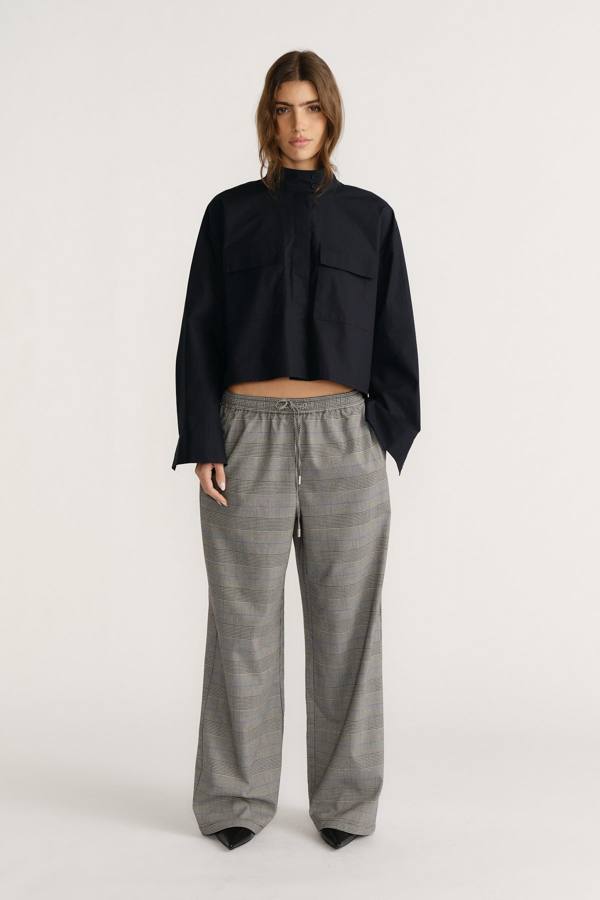Woman wearing a cropped black utility shirt with chest pockets paired with relaxed gray checked wide-leg pants and black shoes