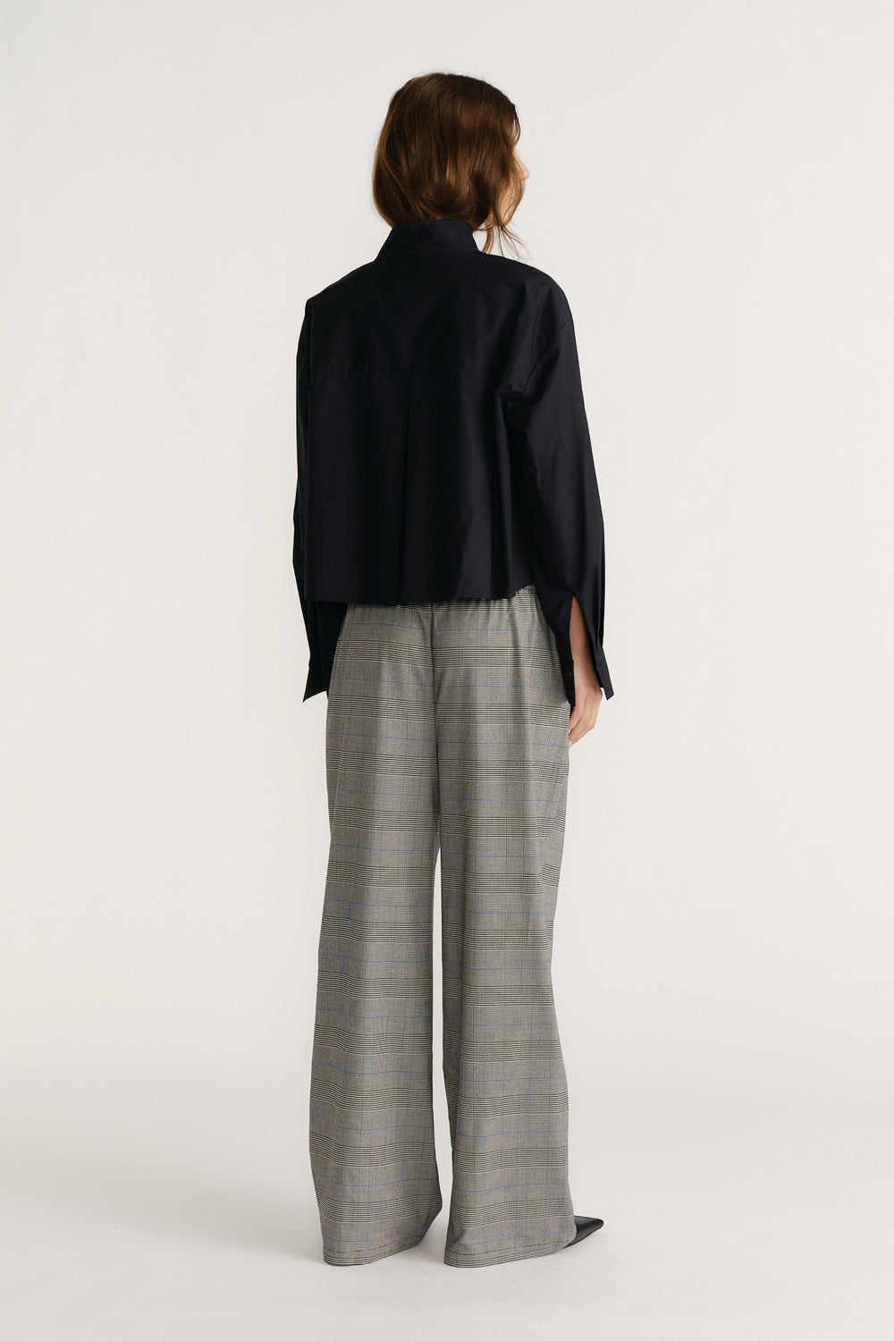 Woman wearing a navy utility-style shirt with long sleeves and grey wide-leg checked trousers viewed from behind