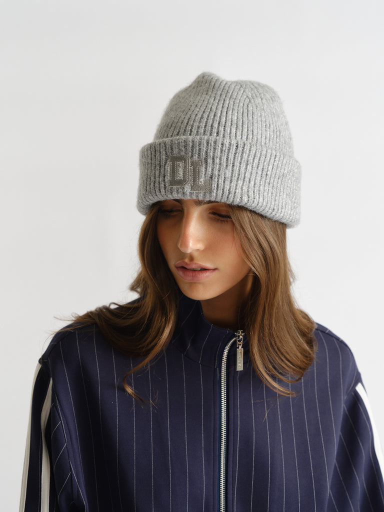 Woman wearing a soft grey ribbed D-luxe Kellie Beanie paired with a navy pinstripe zip-up top for a cozy look