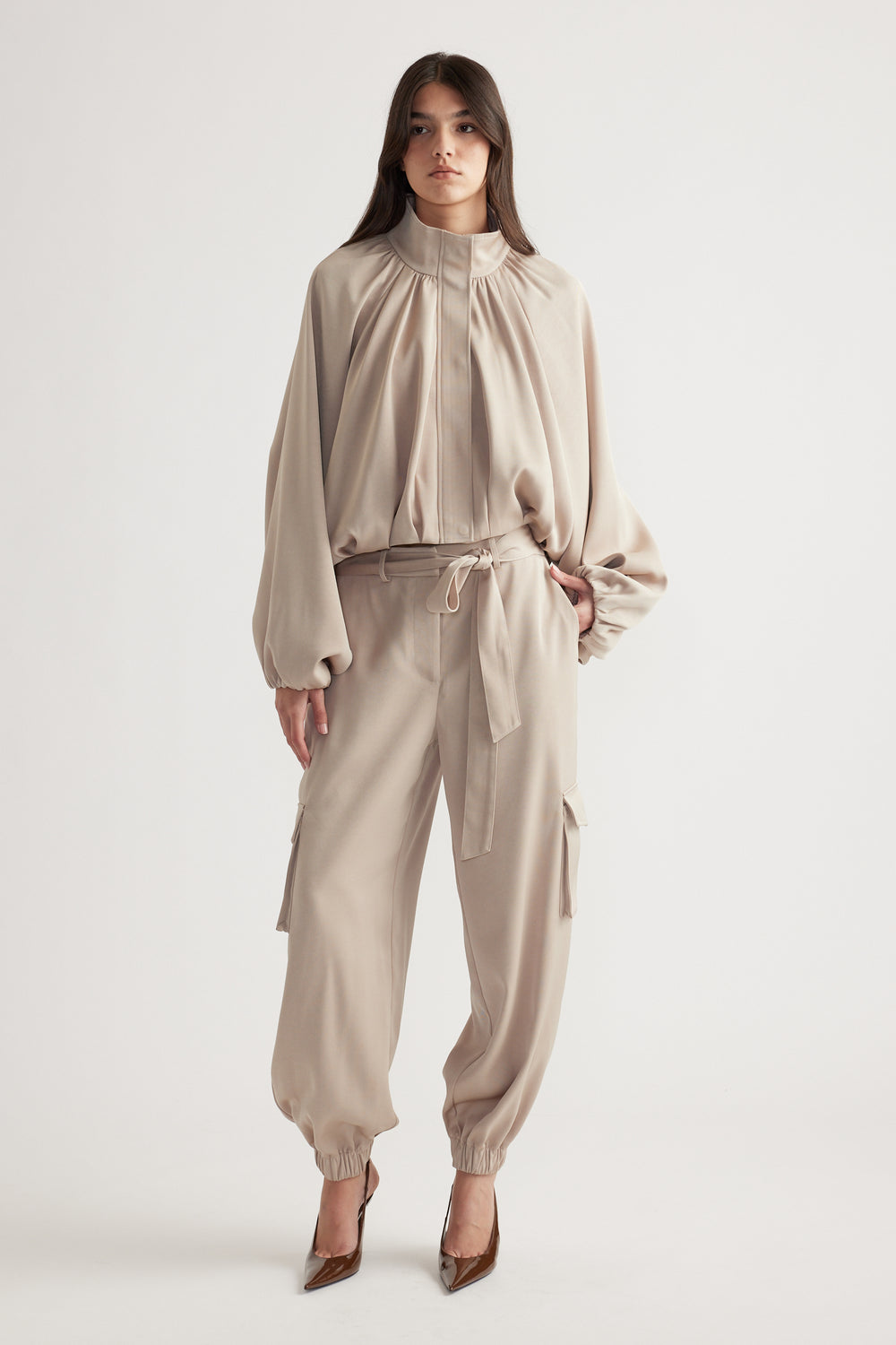 Woman wearing a relaxed biscuit-colored satin bubble jacket with matching cargo-style pants and pointed brown heels